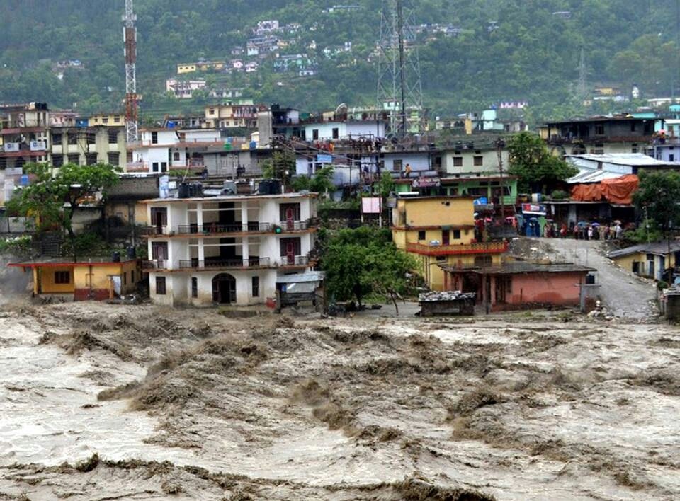 A turbulent, fast-flowing muddy river rushing past a densely built hillside town in Nepal